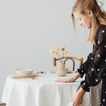 A woman with long blonde hair arranging a table with flowers and elegant dishware.